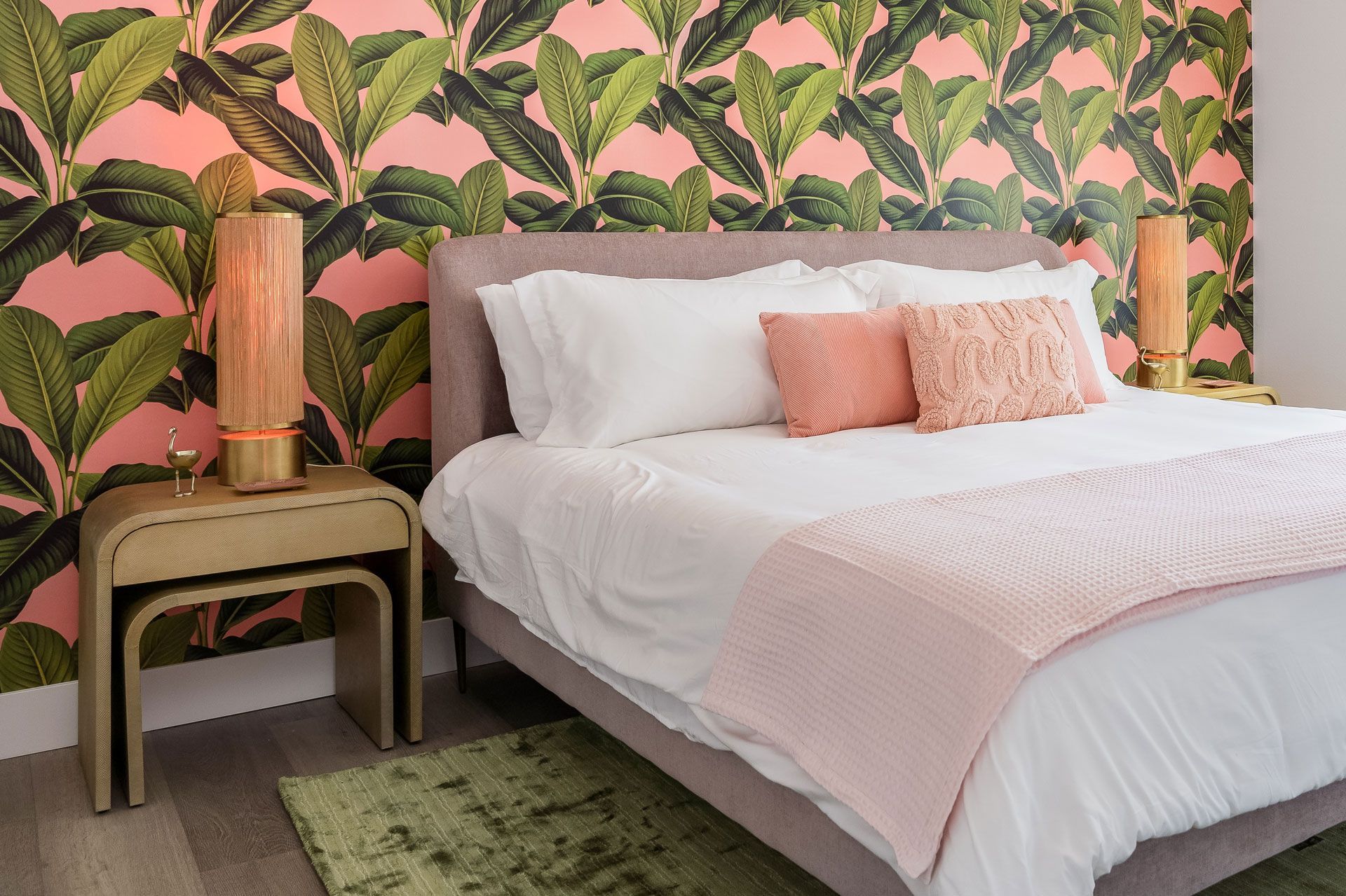 A bedroom with a bed , nightstand , and tropical wallpaper.