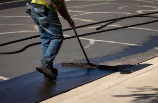 A man is painting a parking lot with a broom.