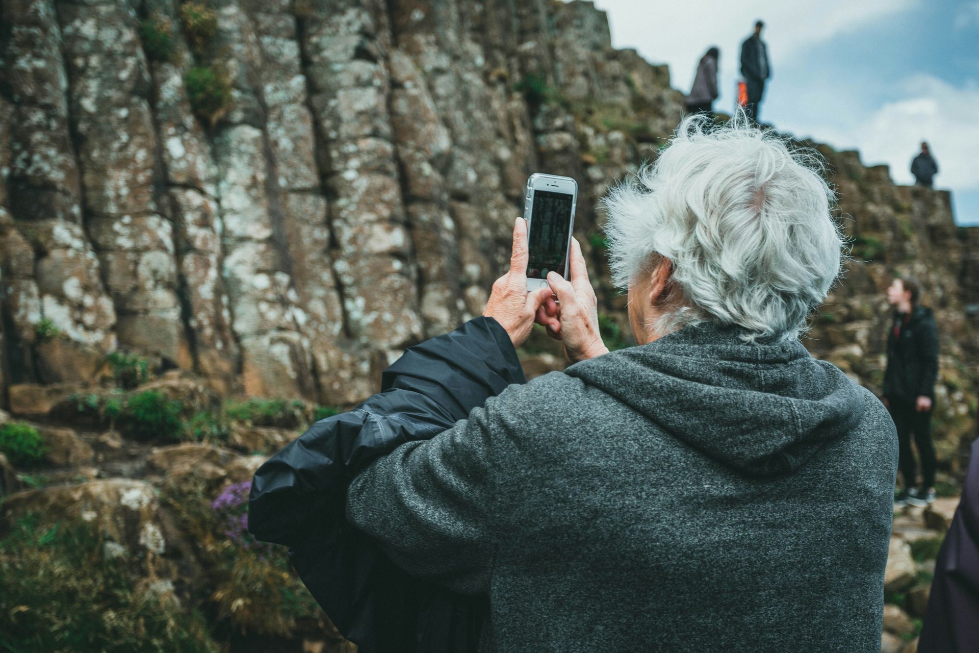 Elderly person taking a photo of the Giant's Causeway in Northern Ireland with a smartphone.