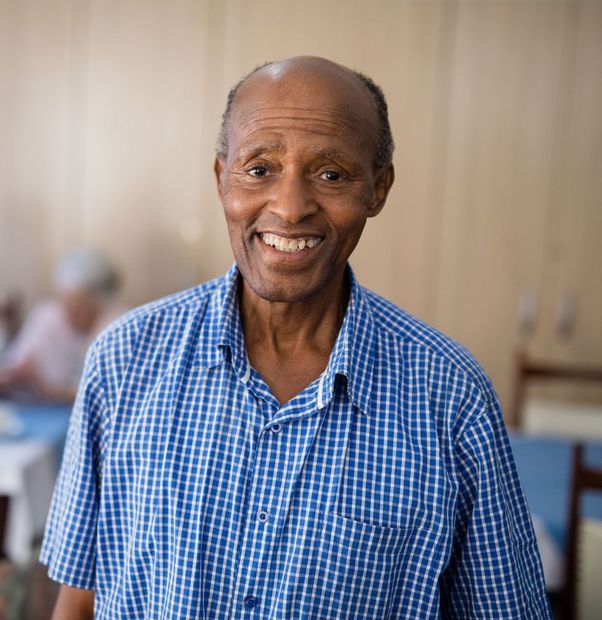 Smiling elderly Black man wearing a blue checkered shirt, indoors.