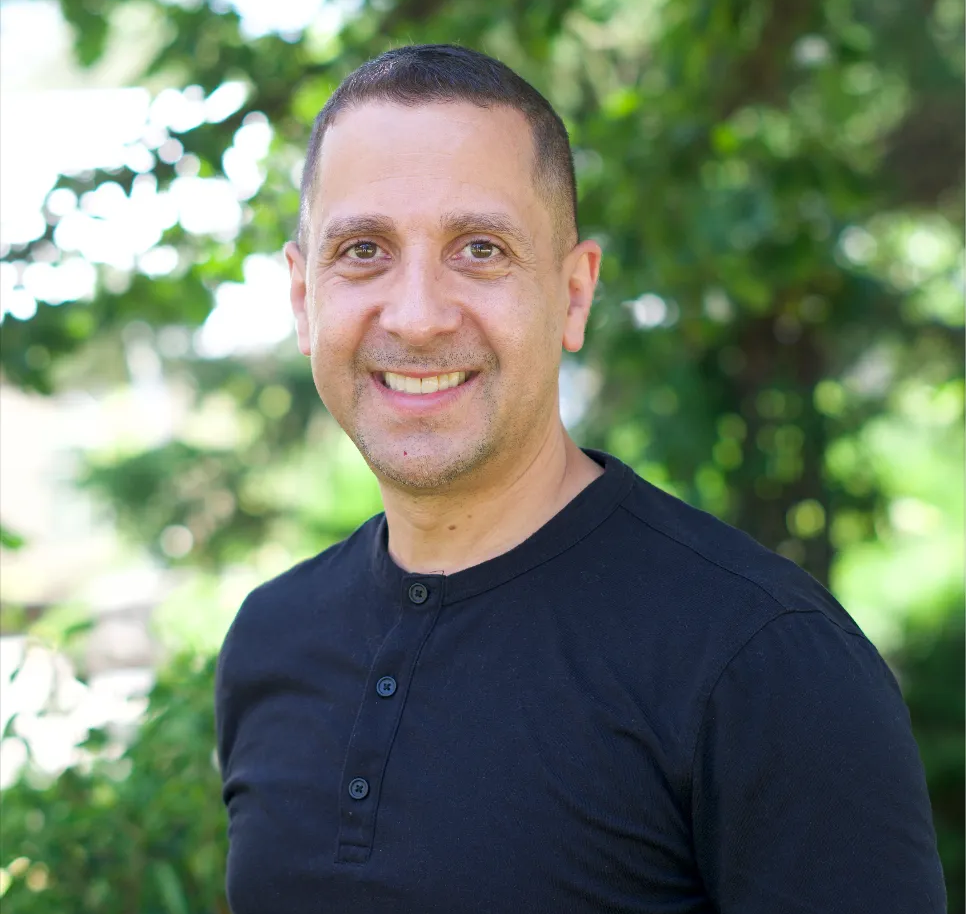 A woman with long curly hair is smiling in front of a tree.