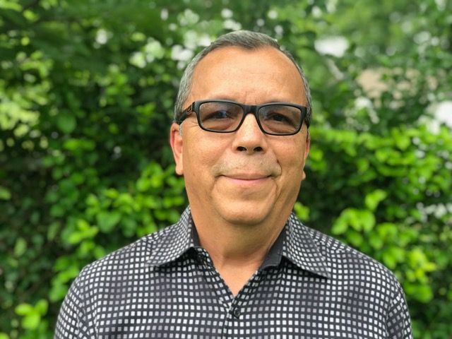 A man wearing glasses and a plaid shirt is smiling for the camera.