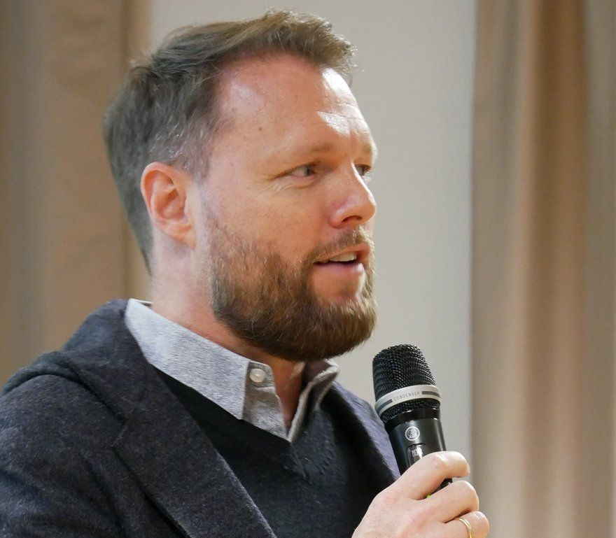 A man in a black shirt is smiling for the camera while standing in front of a building.