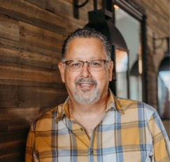 A man with a beard is smiling in front of a brick wall.