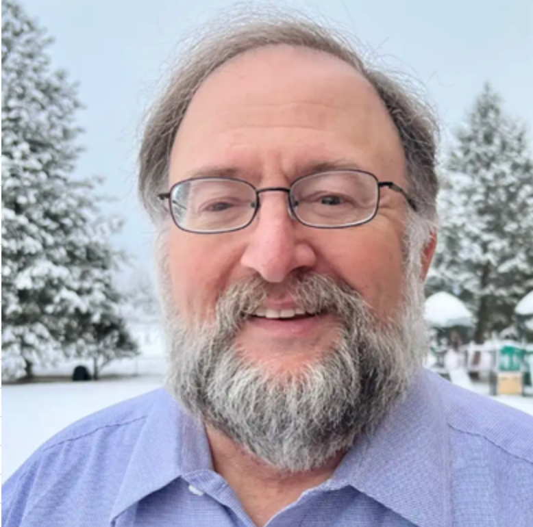 A man with glasses and a beard is smiling in the snow