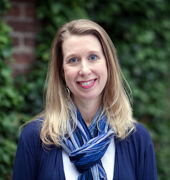 A woman wearing a blue sweater and a blue scarf is smiling for the camera.