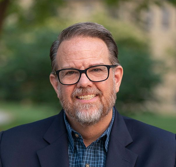 A man wearing glasses and a plaid shirt is smiling for the camera.