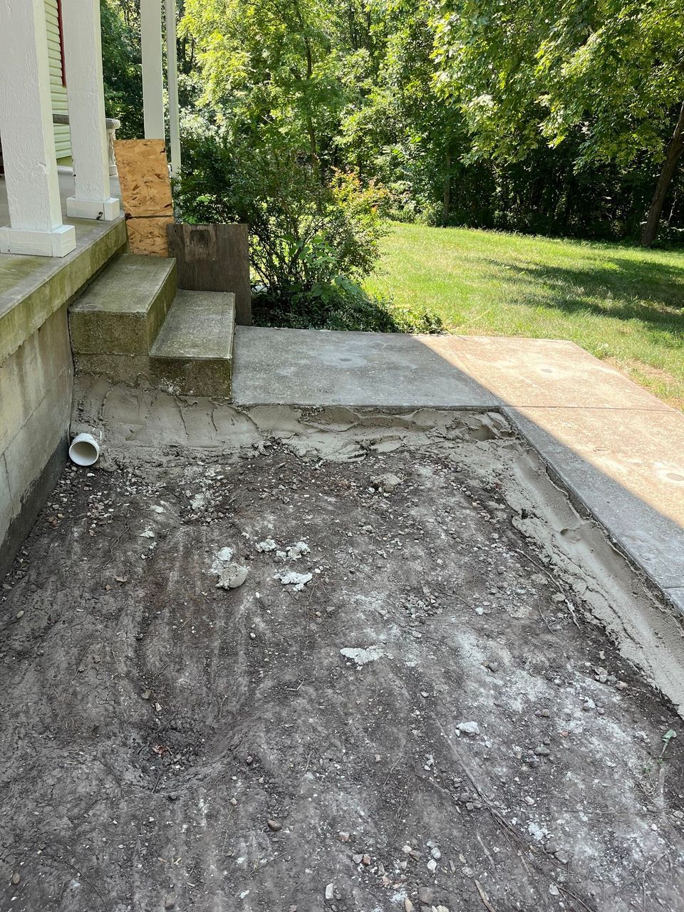 Front porch with a rough gravel surface beside steps, concrete landing, and a grassy yard.
