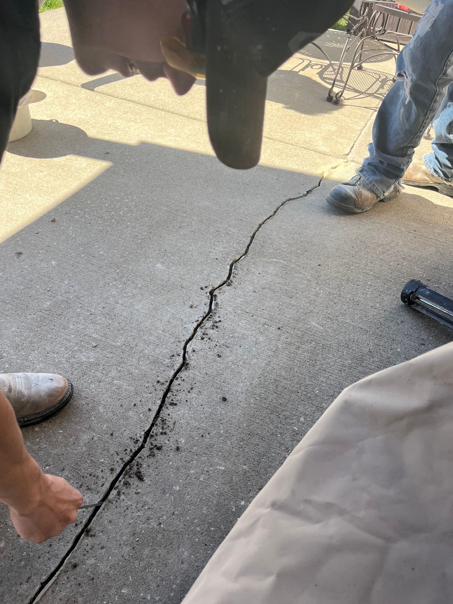 Cracked sidewalk with people standing around, including a person in jeans and a tan bag at right.