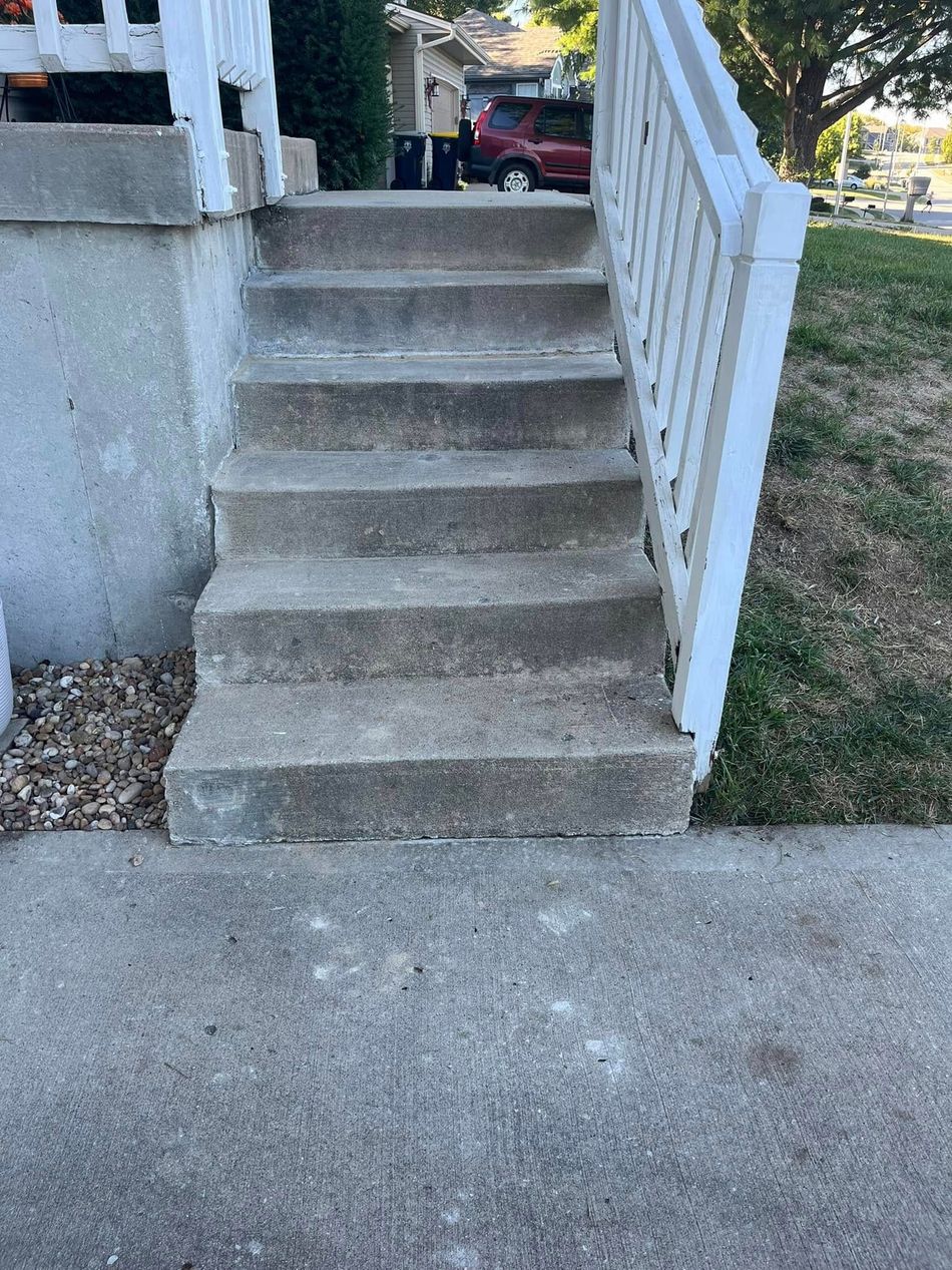 Concrete front steps with a white railing leading up to a porch.