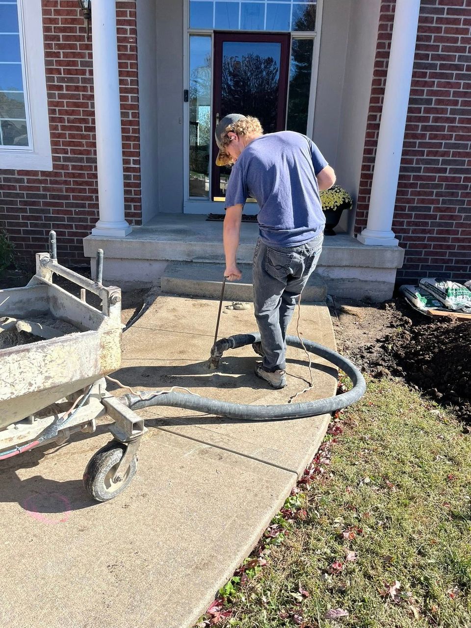 Person using a hose near a brick house entrance, washing a concrete walkway.