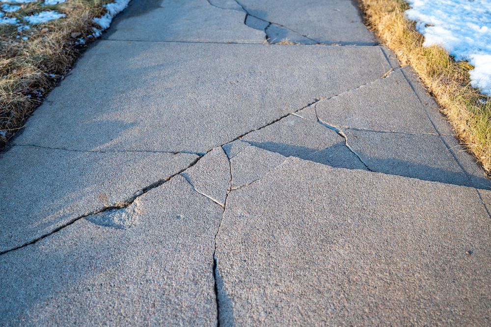 Cracked concrete sidewalk with a large broken section and grass along the edges