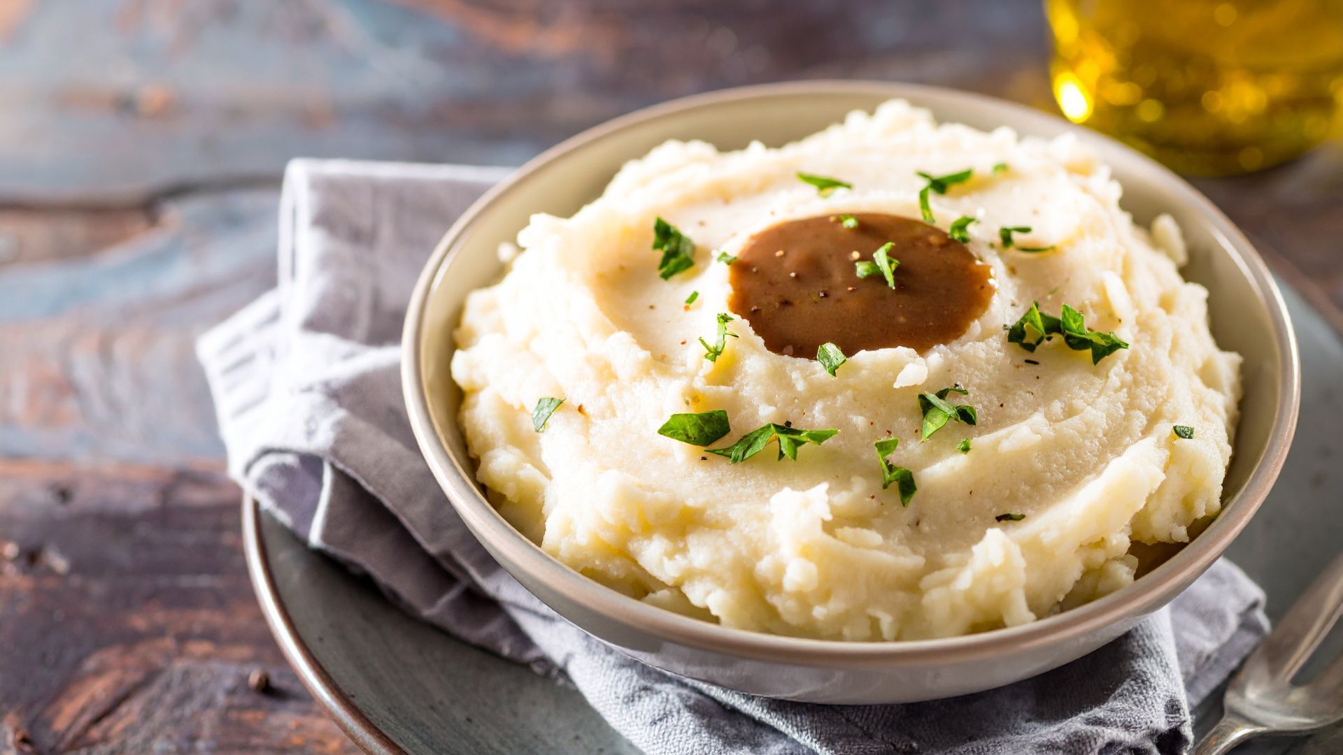 Bowl of mashed potatoes with gravy and parsley garnish.