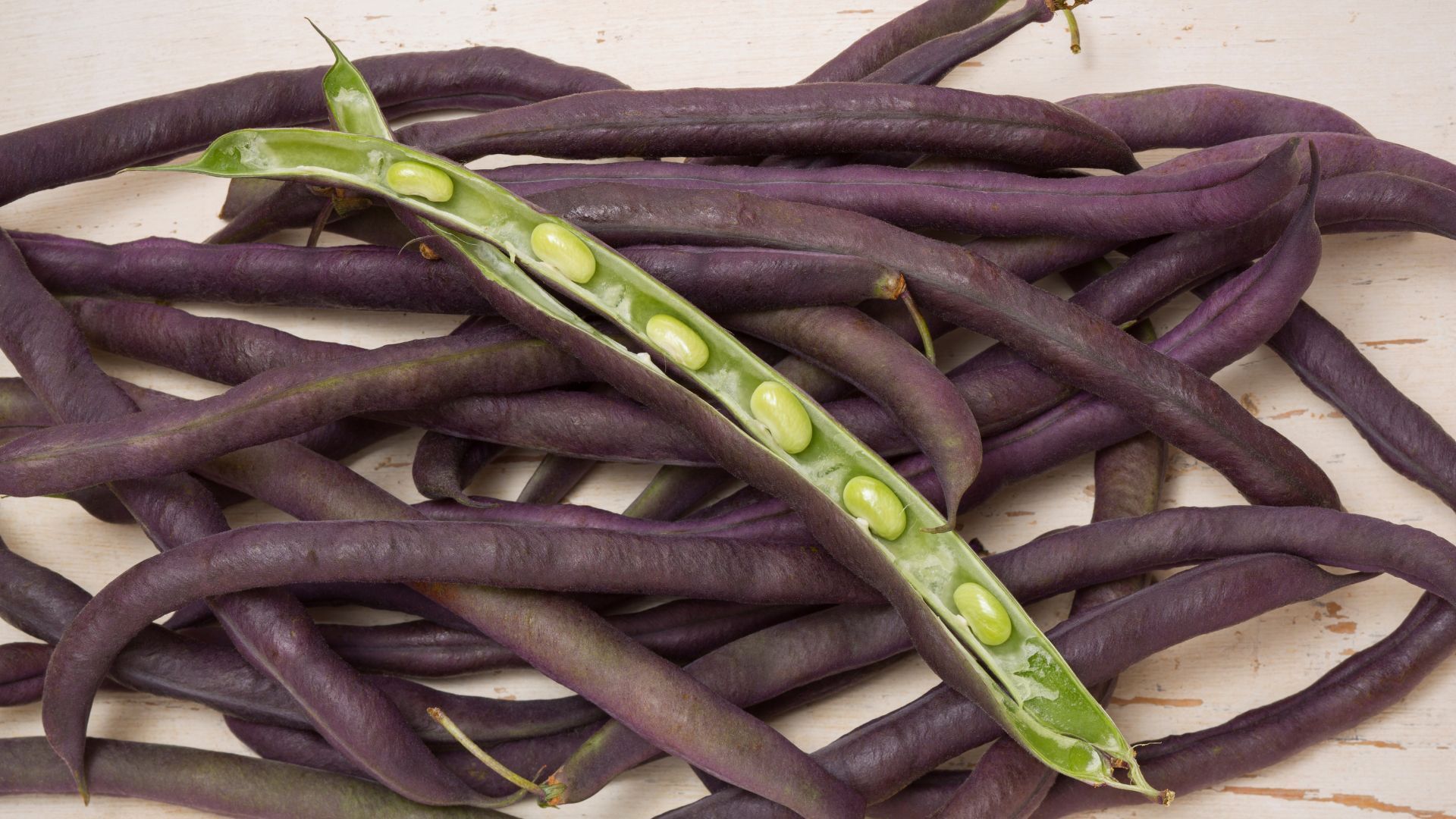 Purple string beans, some whole, some opened, revealing light green beans inside.