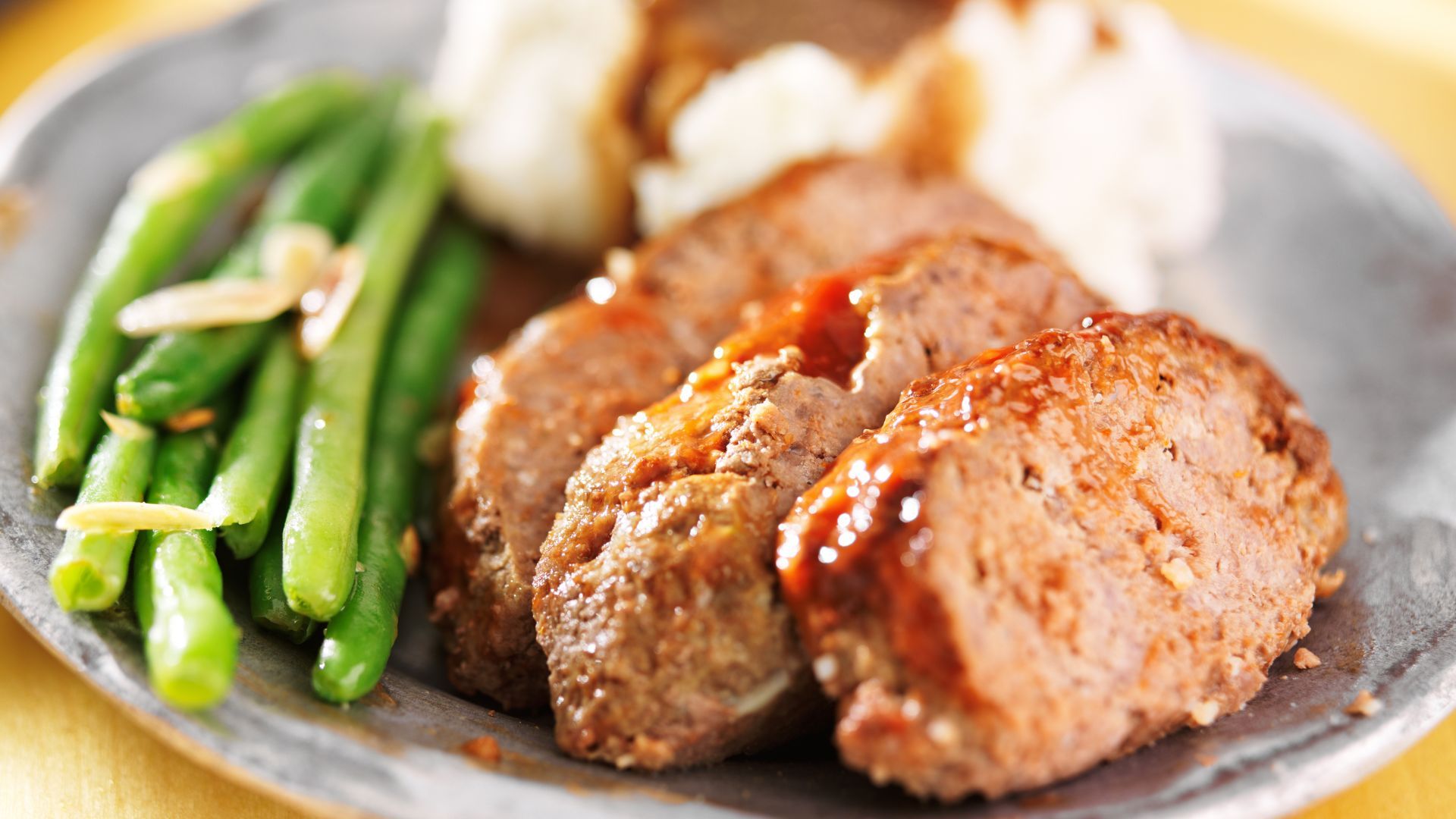 Meatloaf with gravy, mashed potatoes, and green beans on a plate.
