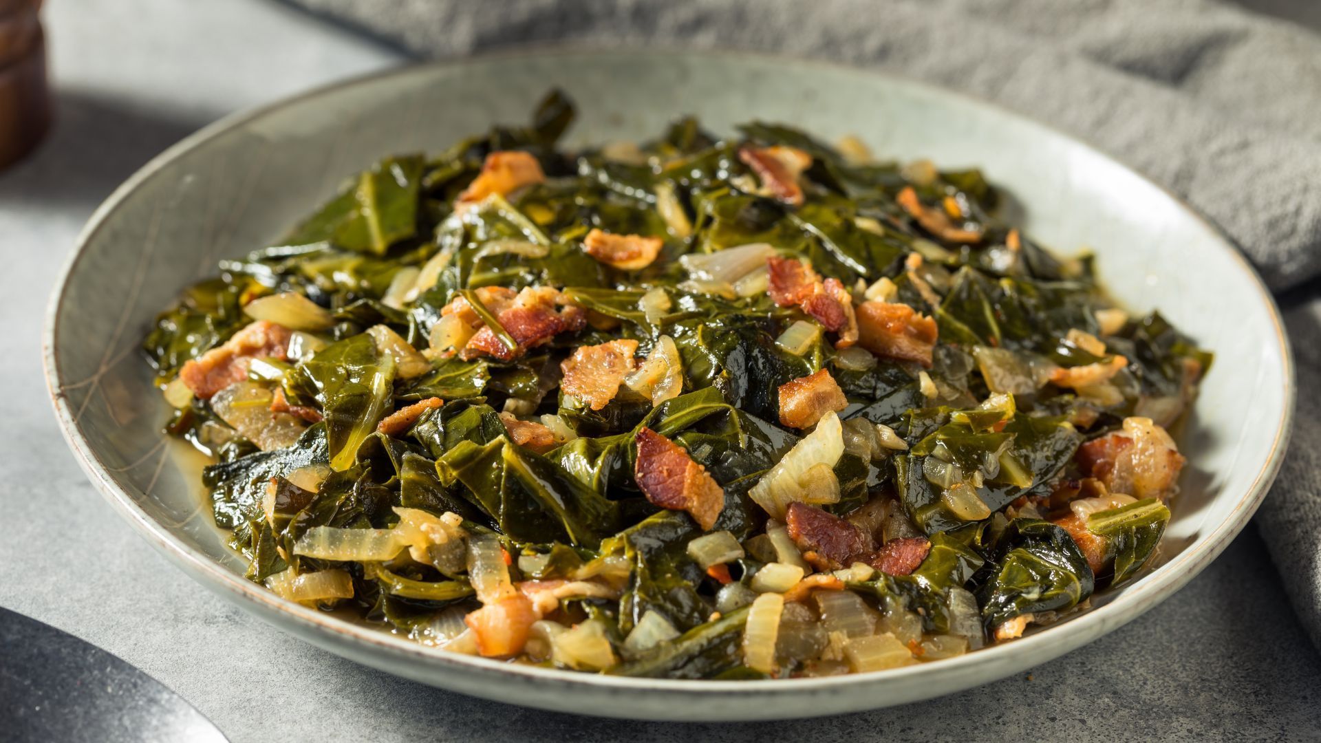 Collard greens with bacon and onions in a light gray bowl.