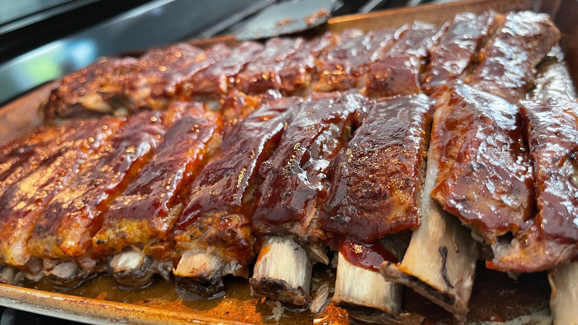 Cooked ribs in a baking pan, glistening with barbecue sauce.