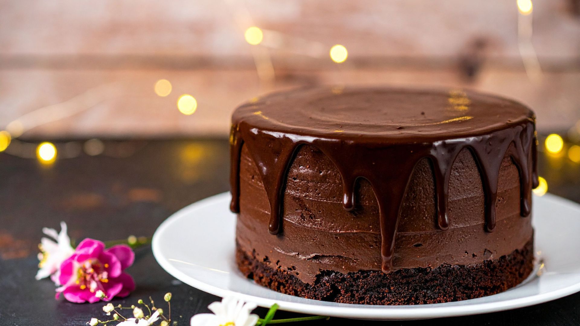 Chocolate cake with chocolate ganache dripping over its sides on a white plate.