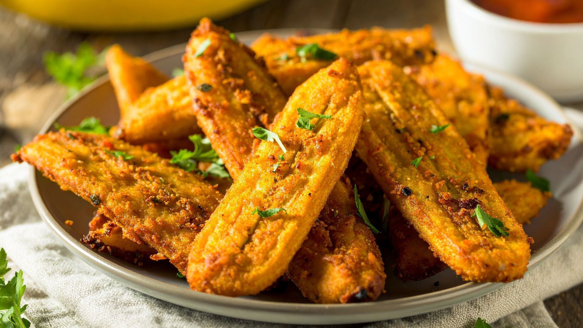 Golden fried plantains, arranged on a plate with fresh parsley, dipping sauce nearby.