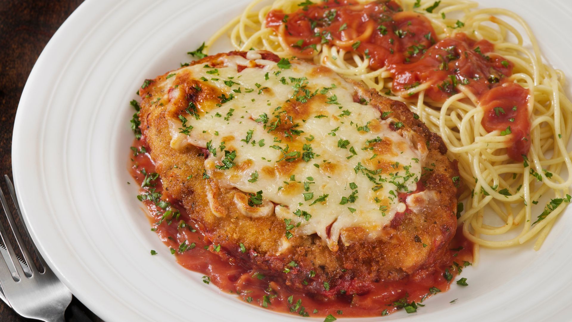 Chicken Parmesan with spaghetti on a white plate.