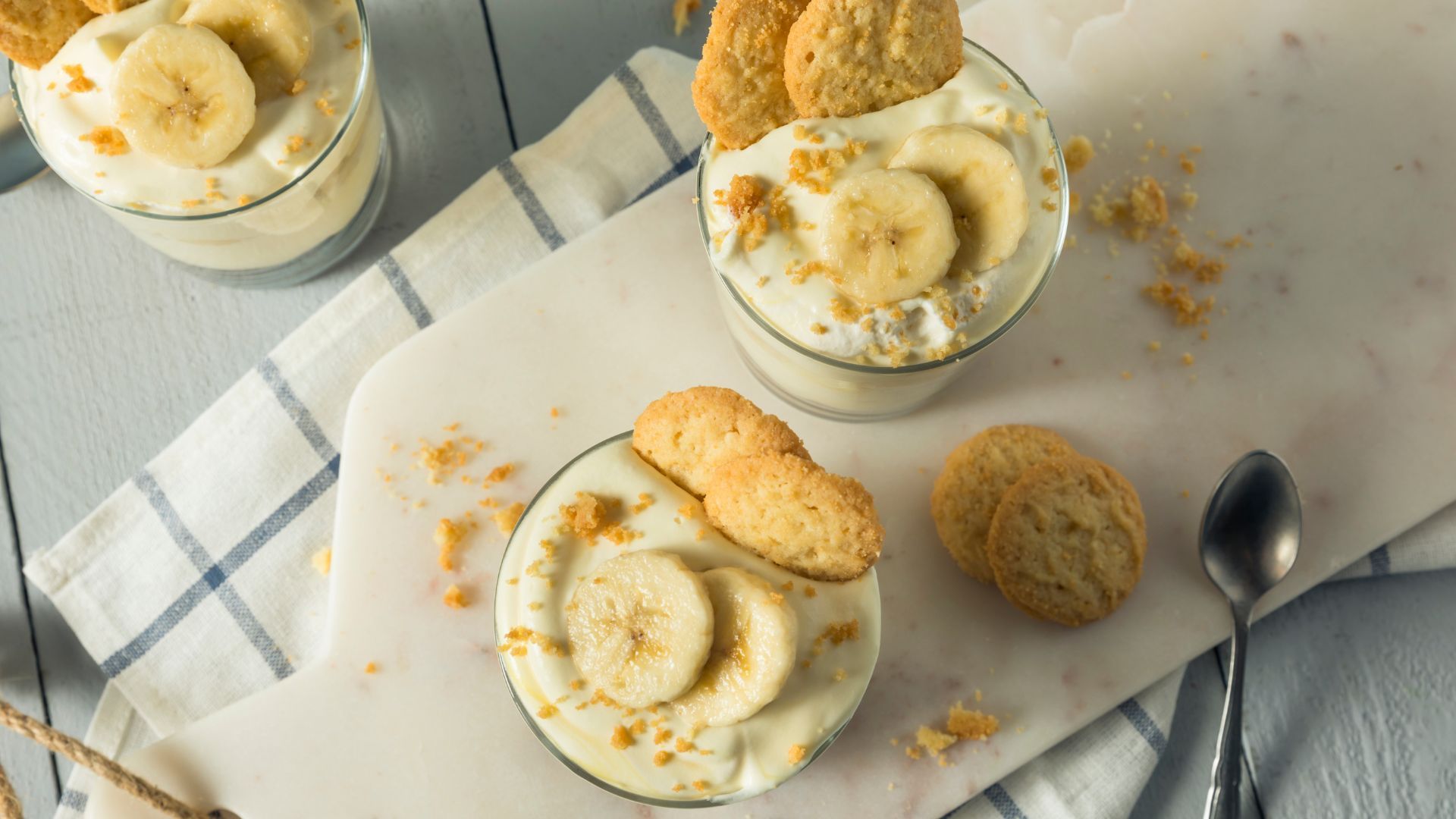 Banana pudding parfaits in clear glasses, topped with cookies and sliced bananas.