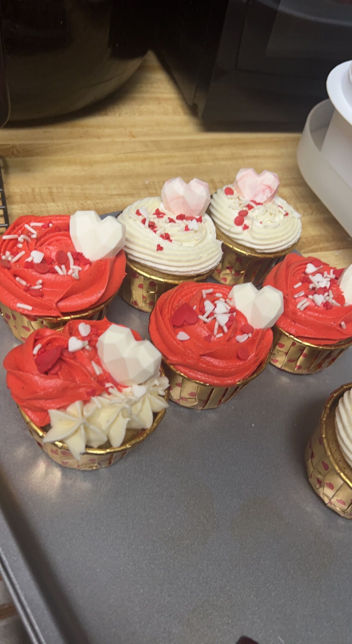 A bunch of cupcakes with red frosting and hearts on them are sitting on a table.