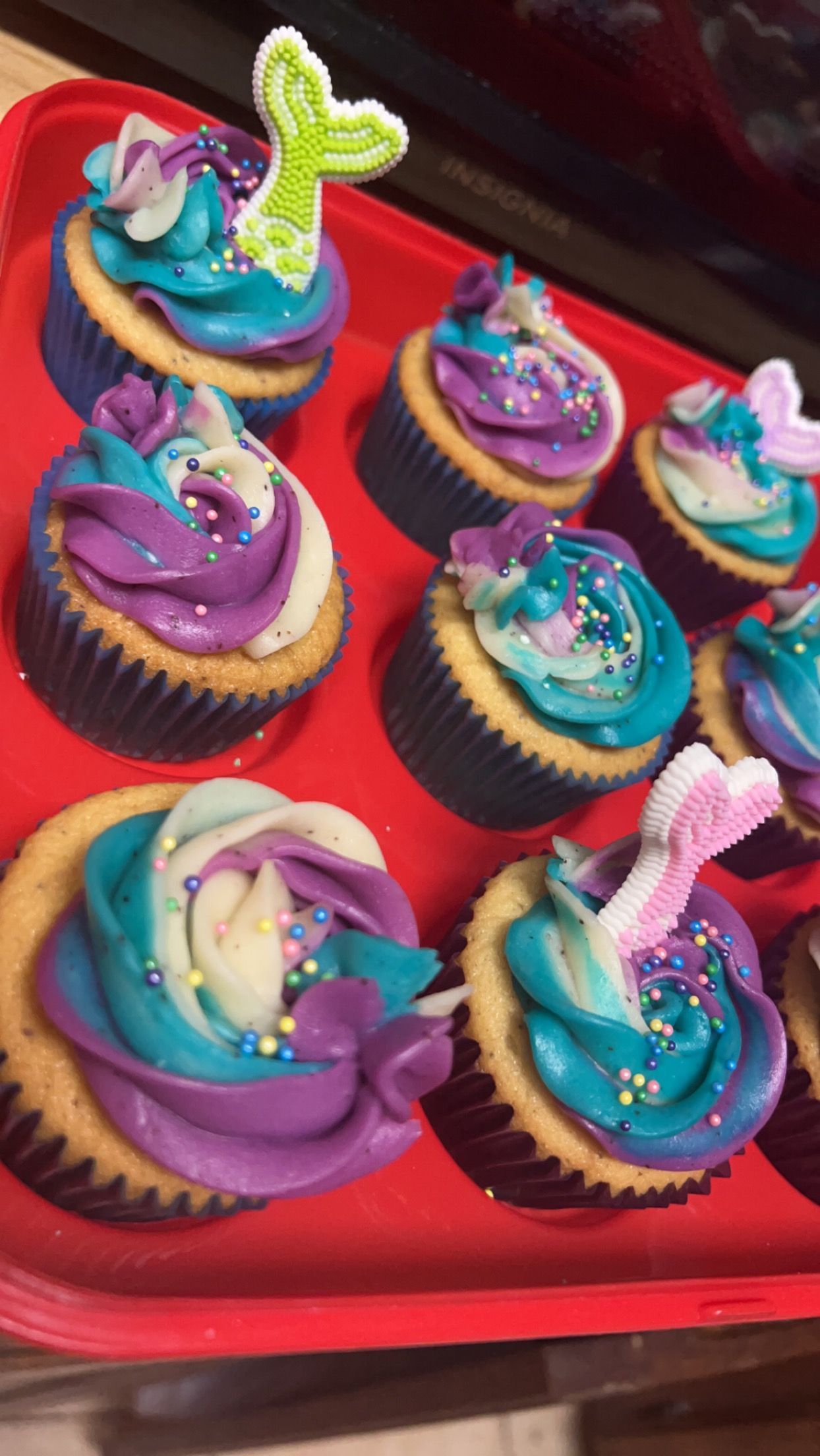 A red tray filled with cupcakes decorated with blue and purple frosting and sprinkles.