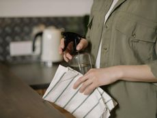Person in green shirt spraying cleaner on a countertop with a striped cloth in a kitchen.