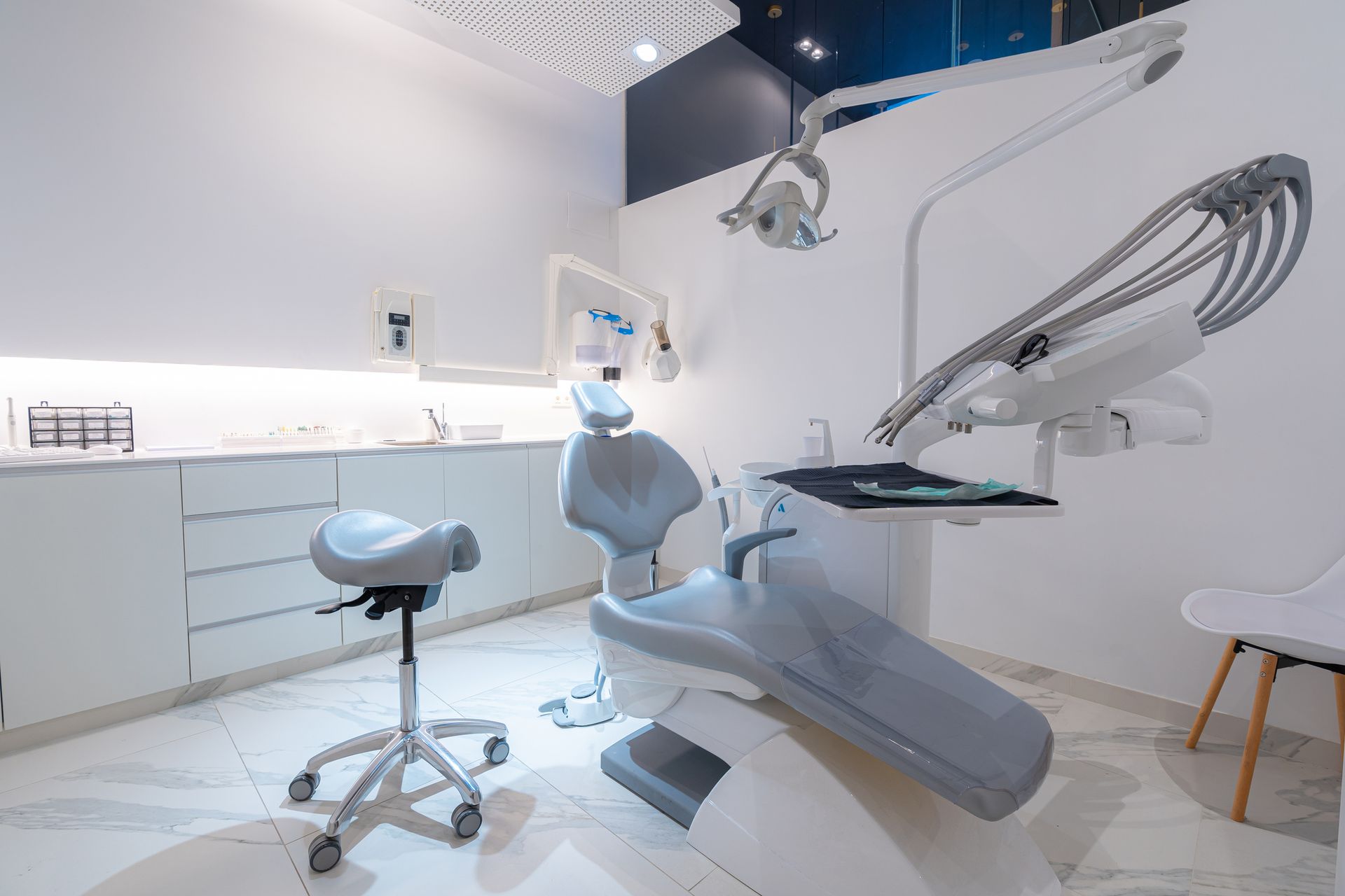 Studio dentistico moderno con pareti bianche, poltrona odontoiatrica grigia e attrezzatura.