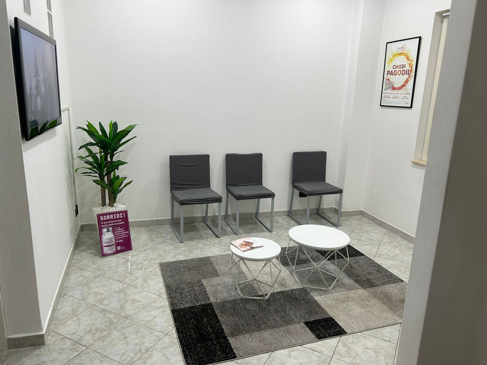 Sala d'attesa con sedie, tavolini, tappeto, piante e opere d'arte.