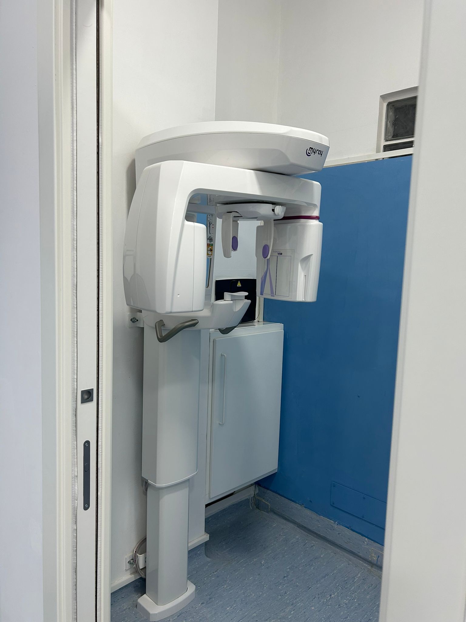 Apparecchio per radiografie panoramiche dentali in una stanza bianca, parete blu sulla destra.