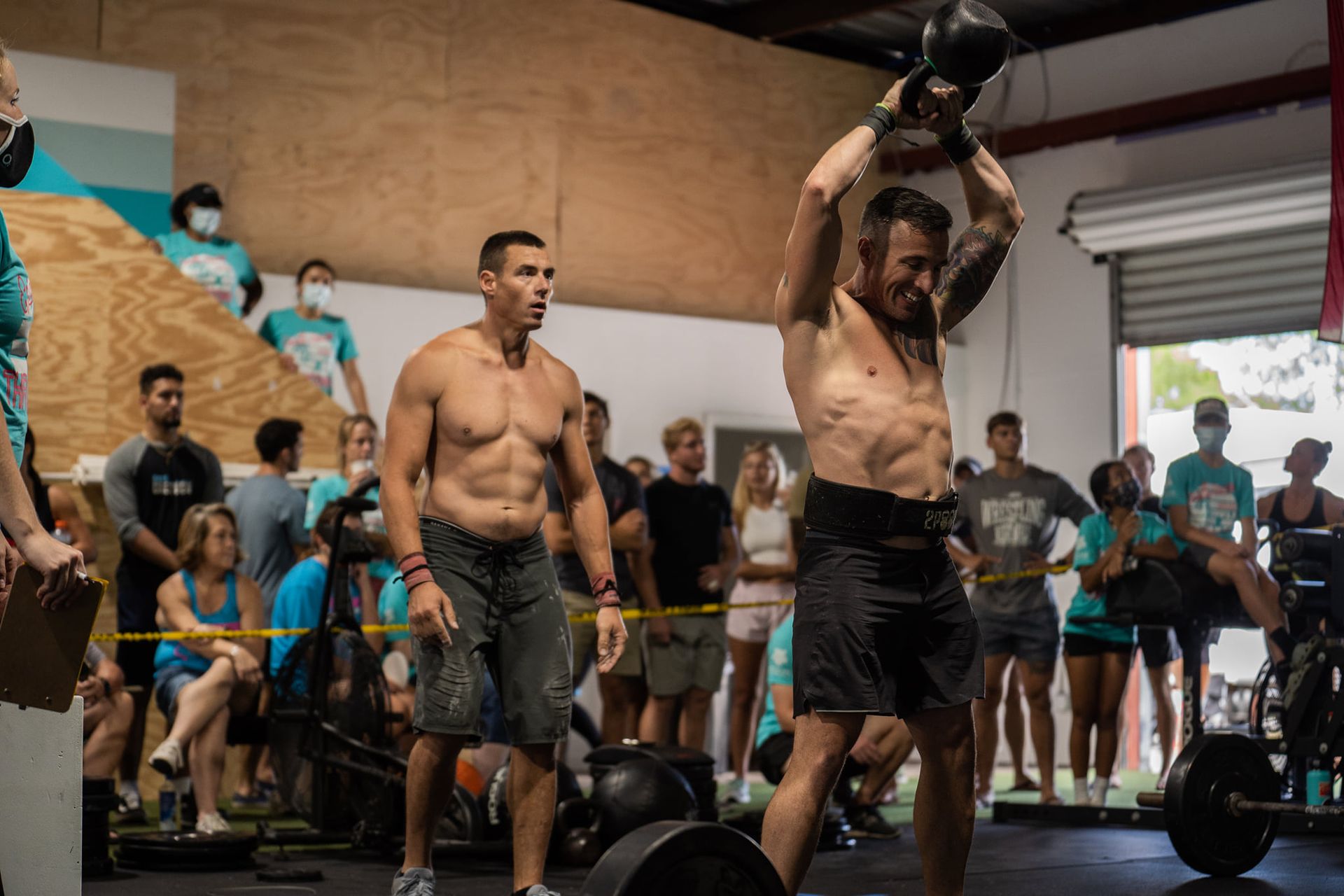 Two men exercising with kettlebells in a gym, one lifting overhead while others watch in the background at the best crossfit gym in Fort Walton Beach, FL