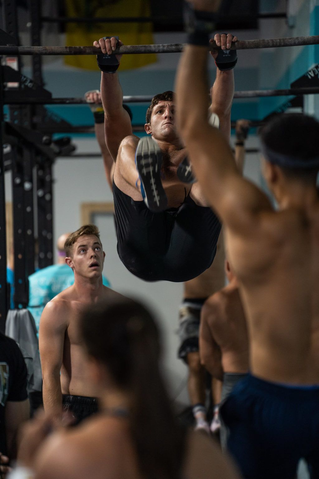 Athlete hanging upside down from a pull-up bar in a gym, surrounded by other workout participants at the best crossfit gym in Fort Walton Beach, FL