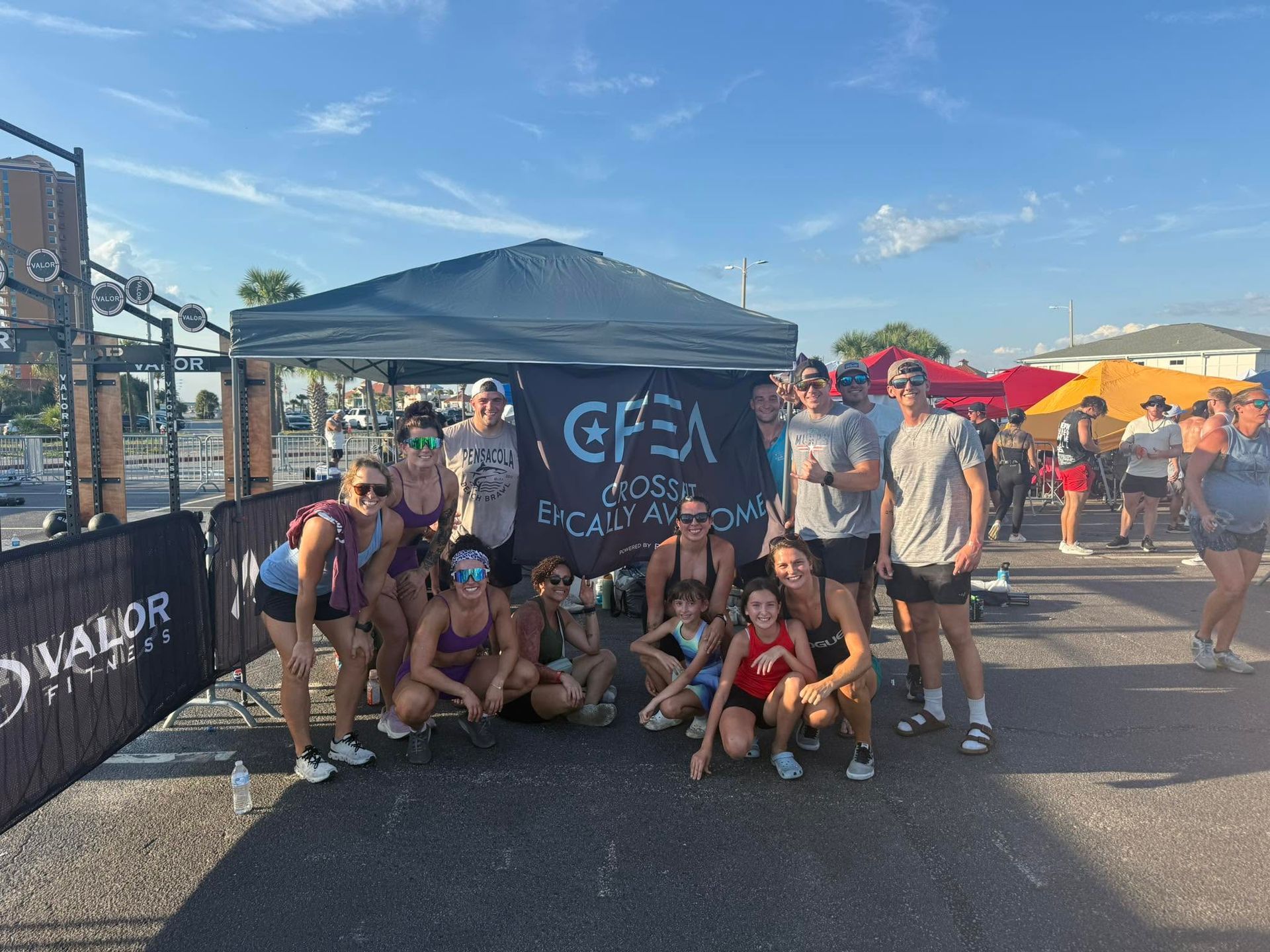 Group posing under a black canopy at an outdoor event, with tents and bright umbrellas in the background at the best crossfit gym in Fort Walton Beach, FL