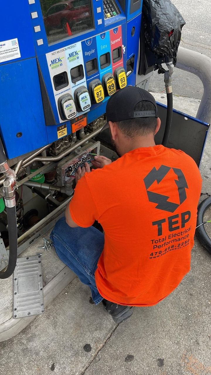 A man in an orange TEP shirt repairs a gas pump, outdoors.