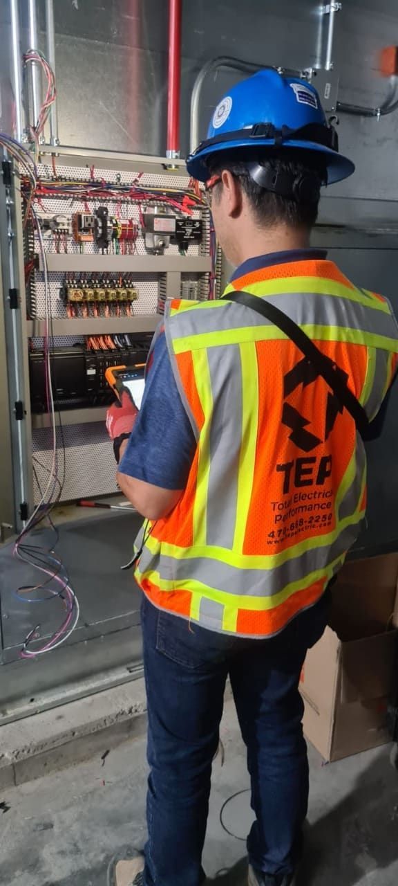 An electrician in a hard hat and safety vest examines electrical equipment.