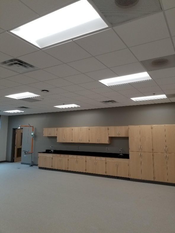 A laboratory or classroom interior with light-colored cabinets, gray wall, and bright overhead lights.