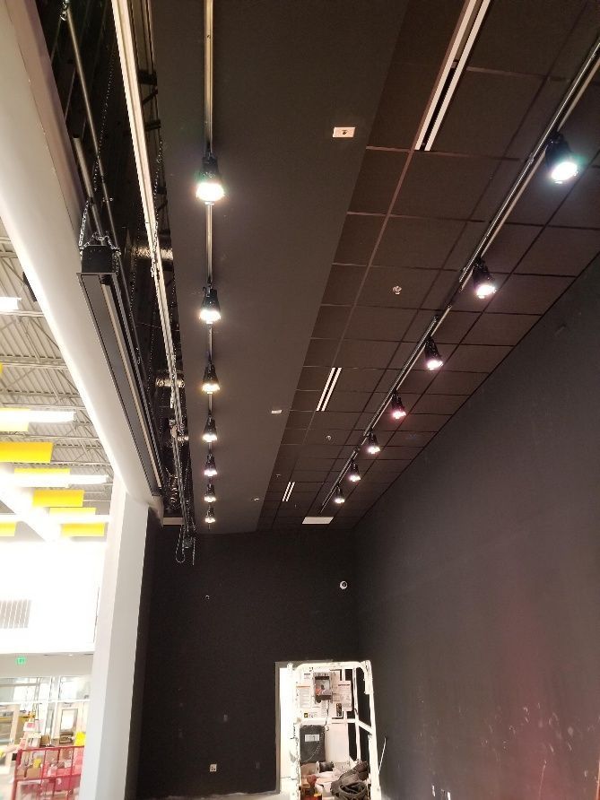 Black ceiling with track lighting illuminating a dark retail space under construction.