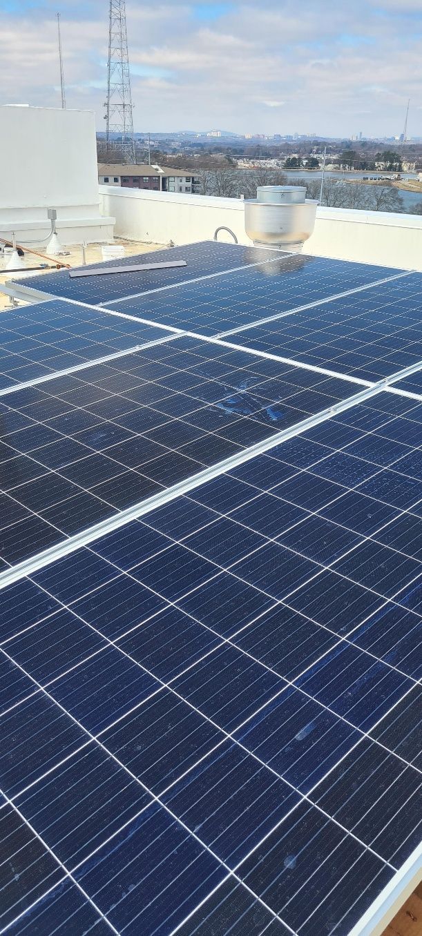 Solar panels on a rooftop, with a cityscape visible in the background under a cloudy sky.