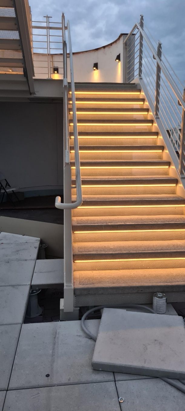 Staircase with lit steps and railings. Beige tones, exterior setting with an overcast sky.