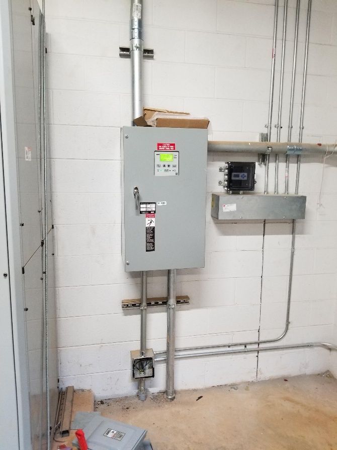 Electrical panel and conduit mounted on a white cinder block wall.