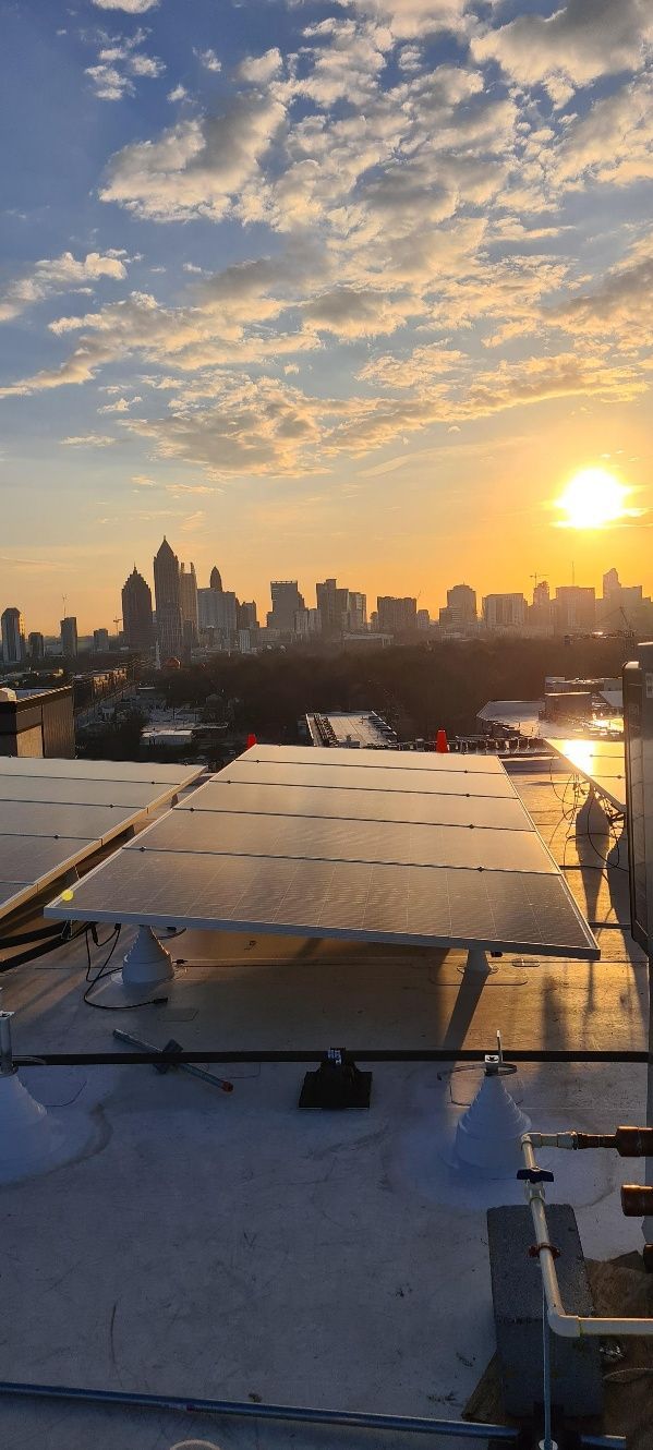 Rooftop view of solar panels with a city skyline at sunset. Golden light bathes the sky and buildings.
