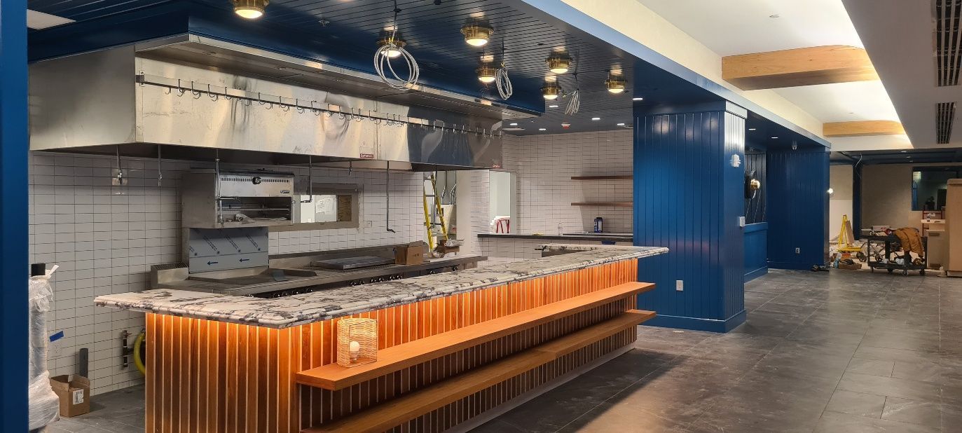 Interior of a partially built restaurant with a kitchen area featuring stainless steel fixtures and a bar.