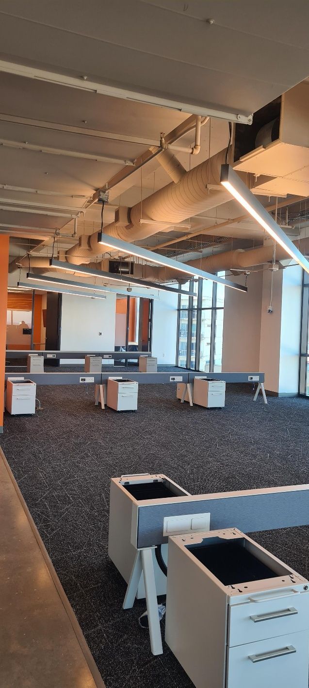 An empty office space with gray carpet, desks, and large windows.