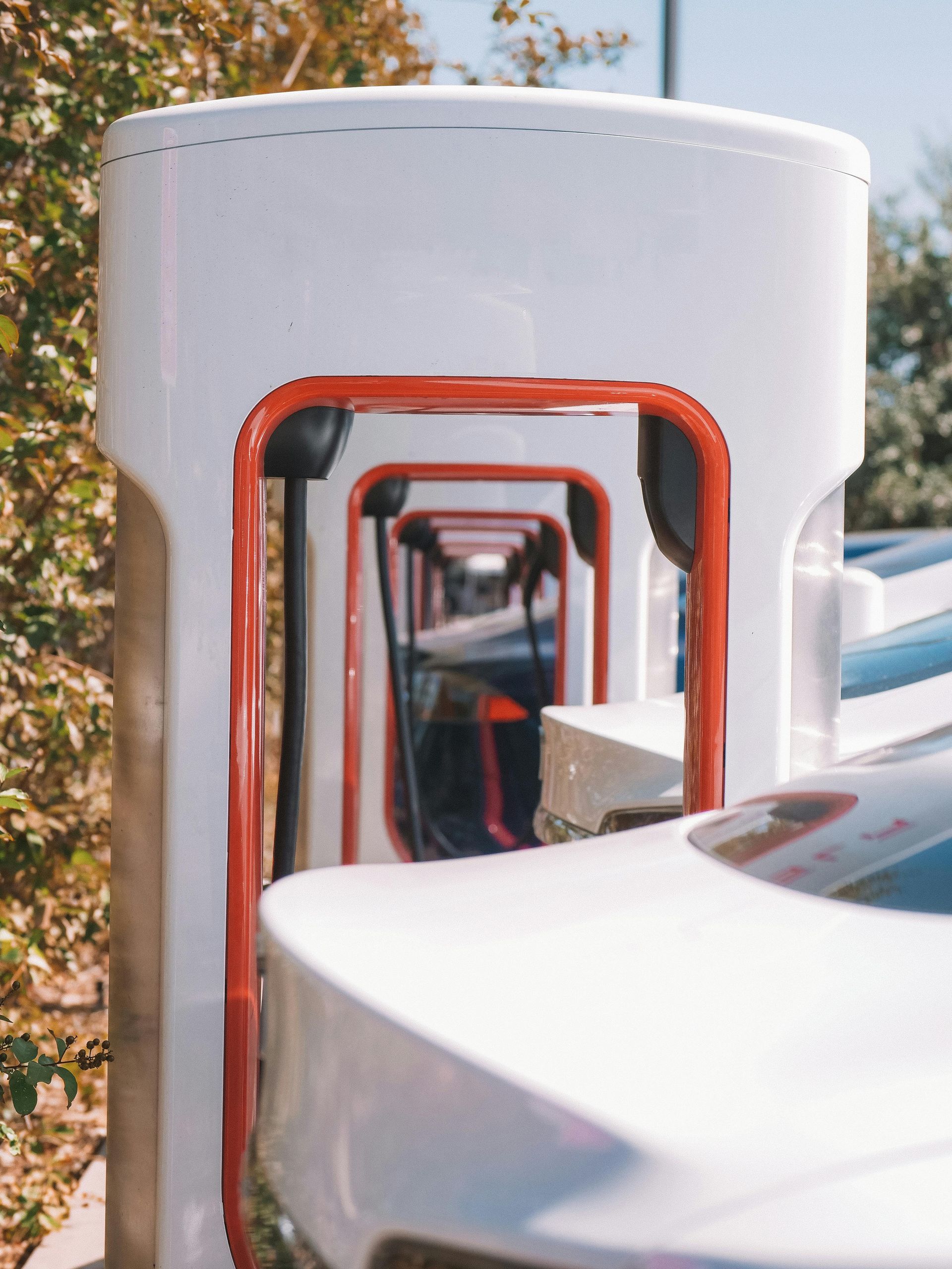 Tesla Supercharger stations lined up outdoors. White and red accents.