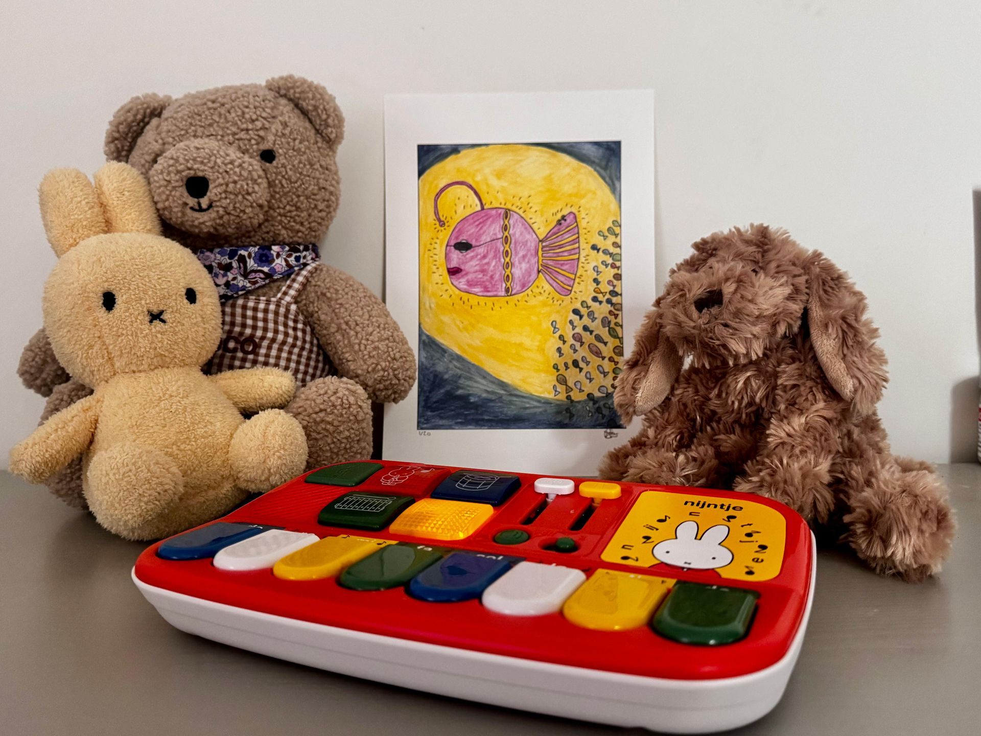 Knuffels en een kindertoetsenbord naast een tekening van een vis op een gele maan.