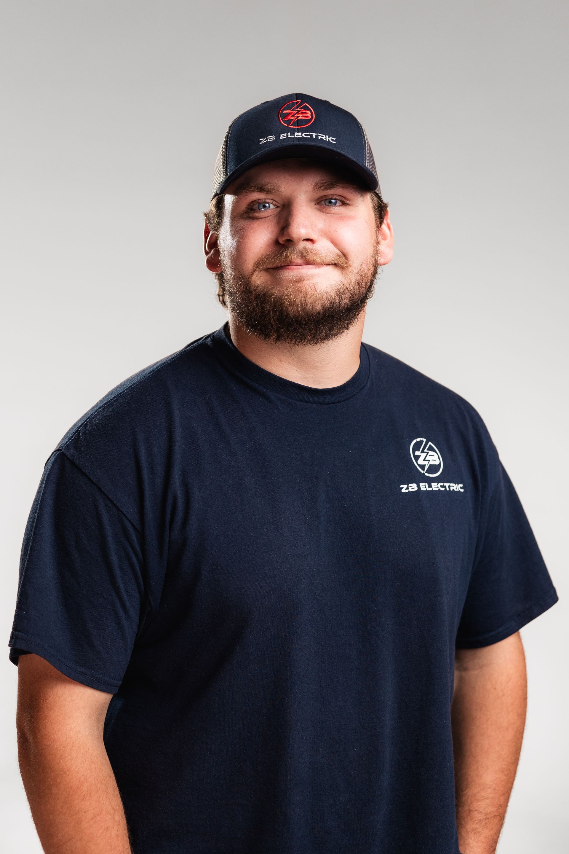 A man with a beard is wearing a hat and a blue shirt.