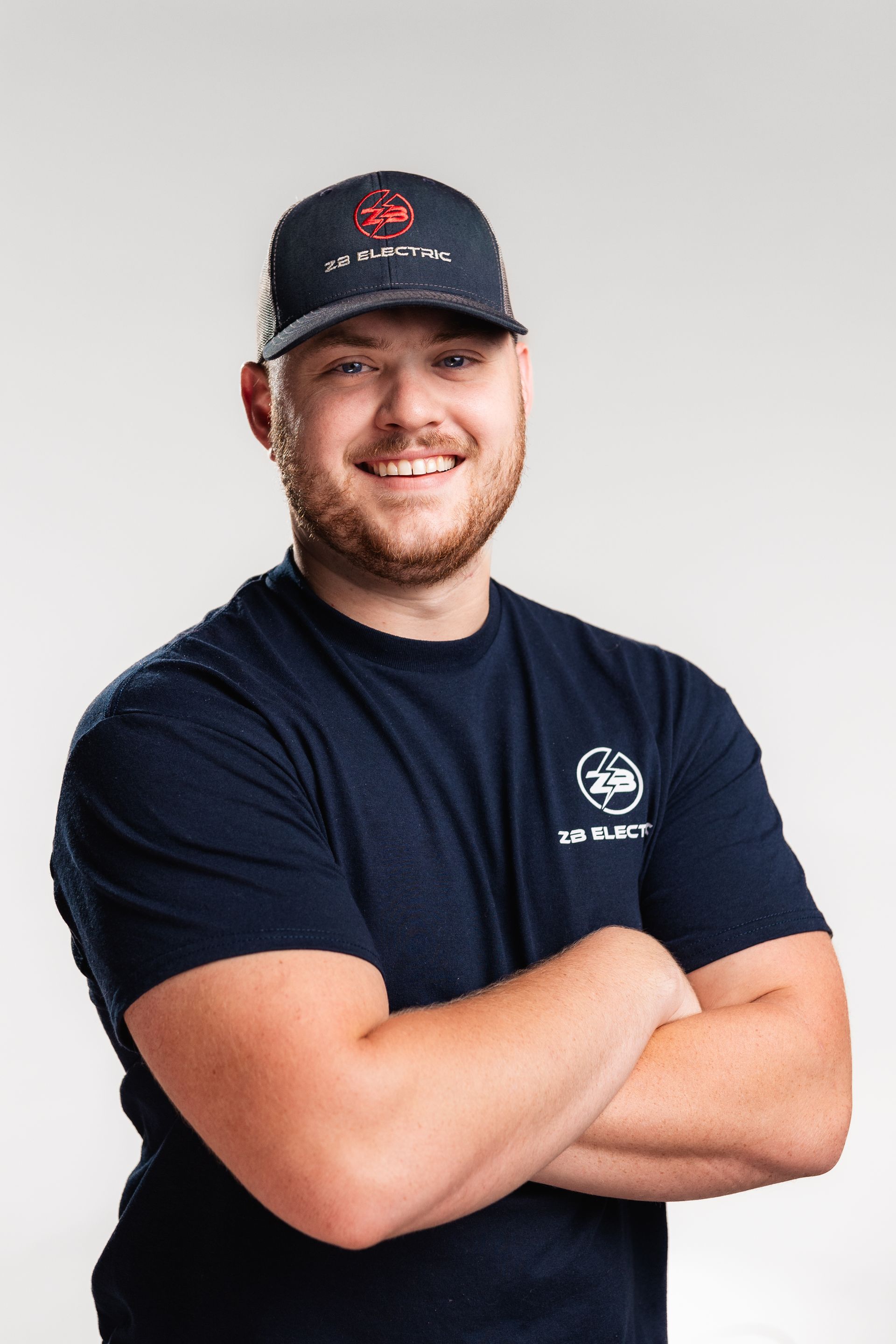 A man wearing a hat and a t-shirt is standing with his arms crossed.