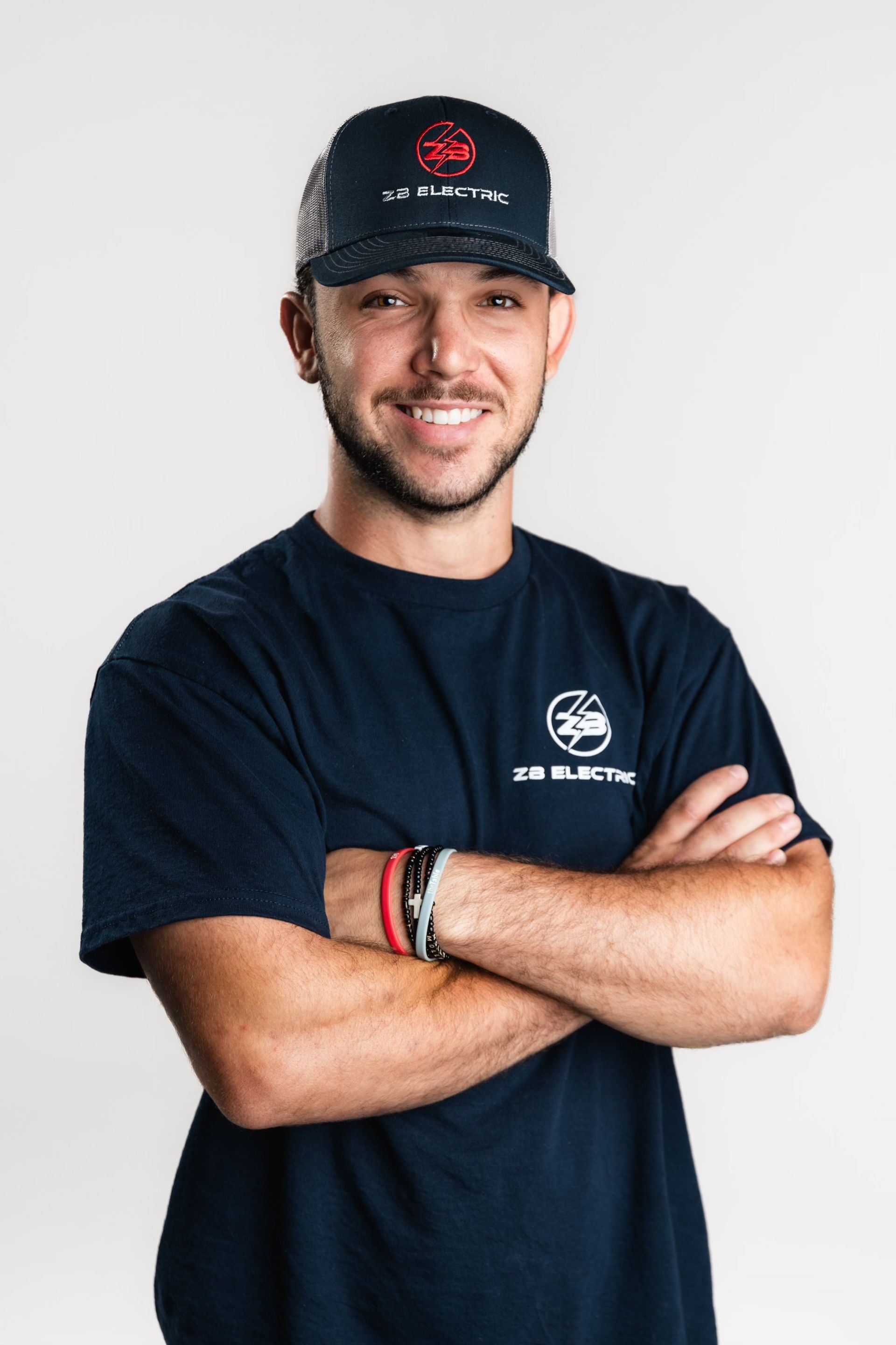 A man wearing a hat and a t-shirt is standing with his arms crossed.