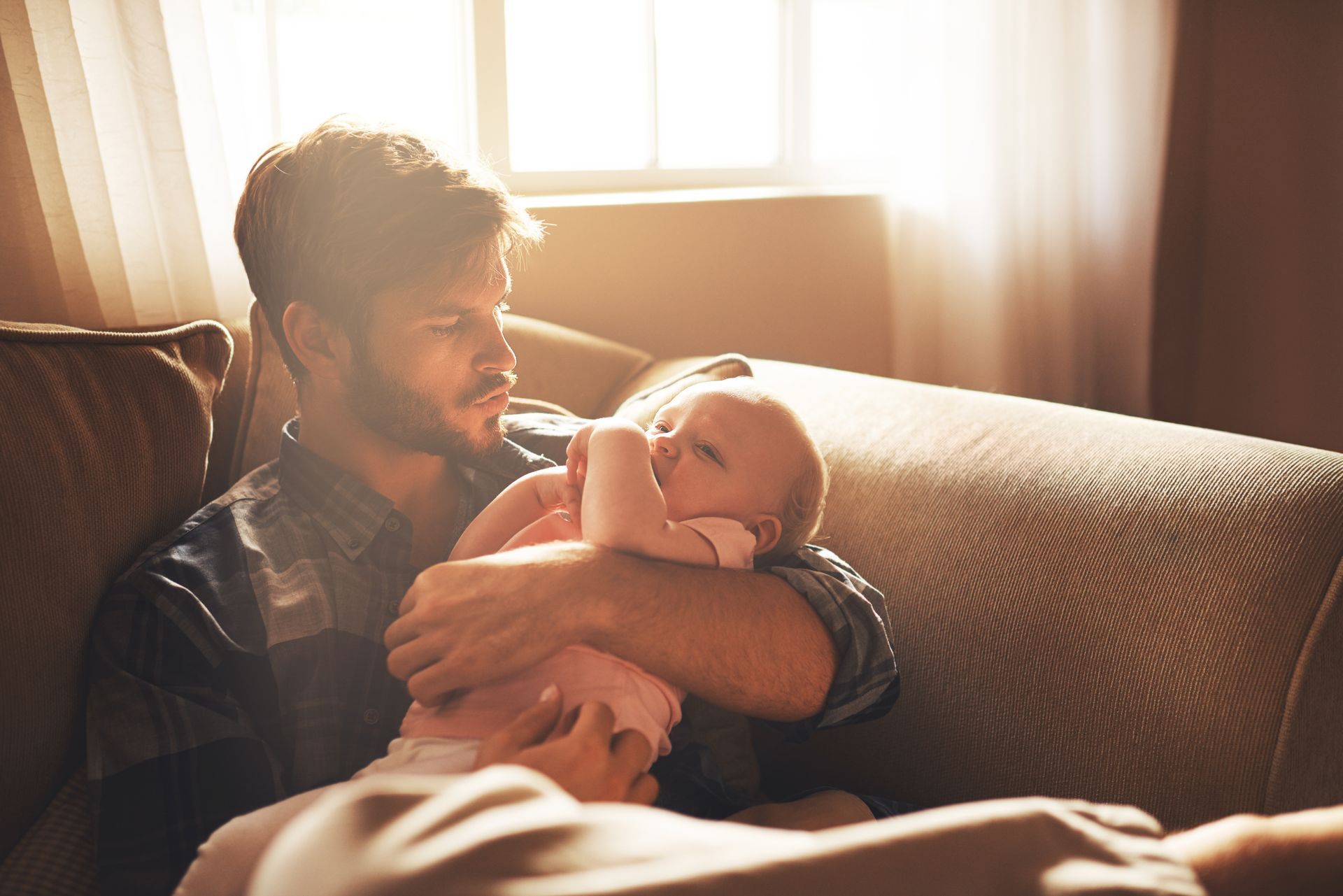 A man is sitting on a couch holding a baby.